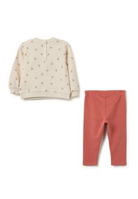 Beige langemouwen top met bloemenpatroon en knoopsluiting bij de nek naast koraalkleurige leggings met een elastische tailleband.