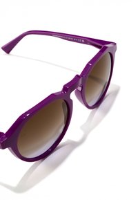 Violetinės plastikinių saulės akinių su apvaliais lęšiais, storu rėmeliu ir unikaliu pjovimo dizainu ant antakio. Rudos spalvos gradientiniai lęšiai.