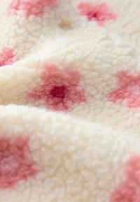 Tissu en polaire doux de couleur crème avec une surface texturée et des motifs floraux roses dispersés, en vue rapprochée.