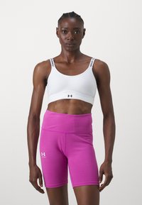 Hvit idretts-bh med svarte logo-stropper, kombinert med høy-midje rosa shorts laget av et glatt, elastisk materiale.