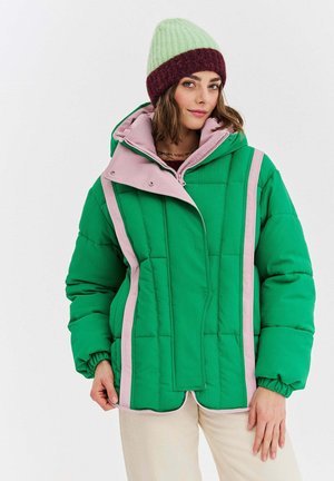 Zielona pikowana kurtka z różowymi akcentami, z wysokim kołnierzem, zapięciem na zatrzaski i prążkowaną teksturą. Model nosi zieloną i bordową czapkę typu beanie.