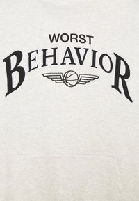 Lichtgrijze hoodie met een voorzak. Voorzien van "WORST BEHAVIOR" in vetgedrukte zwart-witte letters en een basketbalgrafiek met vleugels.