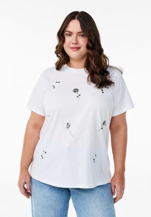 T-shirt blanc en coton à manches courtes, avec broderie florale multicolore et coupe décontractée, associé à un jean bleu clair.