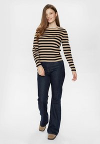 Prugasta dugorukava majica u bež i crnoj boji, uparena sa tamnoplavim trapeznimfarmerkama. Outfit se odlikuje jednostavnim, prilagođenim dizajnom.