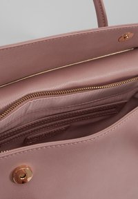 Růžová kožená kabelka uvnitř s jedním zipovým kapsou a sloty na karty, se zlatým zipem a kování, hladká textura.