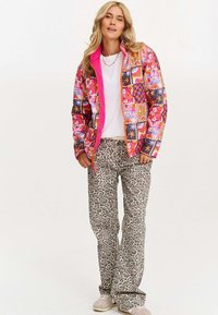 Kolorowa kurtka puchowa z kwiatowymi i geometrycznymi wzorami, różowy prążkowany kołnierz. Beżowe spodnie w leopardzi wzór, neutralne sneakersy.