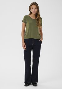 Camicia olive green a maniche corte abbinata a jeans svasati blu scuro, che mette in risalto una vestibilità rilassata e una texture leggera e liscia.