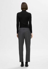 Un turtleneck noir à manches longues associé à un pantalon gris sur mesure. Le pantalon présente deux poches arrière et un design à jambe droite. Des chaussures noires complètent le look.
