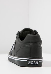Zapatilla negra con textura de cuero suave, diseño bajo, acentos blancos y suela de goma a rayas. Presenta el logo 'POLO' en el talón.