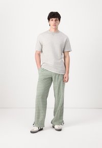 Un tricou din bumbac gri, cu guler rotund și mâneci scurte, asortat cu pantaloni în carouri verzi și albe. Pantofi cu un mix de gri și alb.