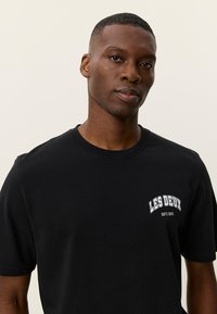 Μαύρο βαμβακερό t-shirt με στρογγυλή λαιμόκοψη και κοντά μανίκια, με λευκό κείμενο "LES DEUX" και έτος ίδρυσης τυπωμένα στο μπροστινό μέρος.