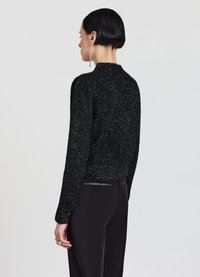 Schwarzer, flauschiger Strickpullover mit rundem Ausschnitt und langen Ärmeln. Der Stoff hat eine strukturierte Oberfläche, kombiniert mit maßgeschneiderten schwarzen Hosen.