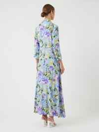 Cvetna maksi obleka iz svetlo modrega materiala, s purpurnimi in zelenimi botanskimi motivi, s tremi četrtinami rokavov in širokim krojem. Bele blok petke.