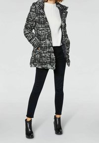 Kurtka puchowa w czarno-białą kratę z kapturem i bocznymi kieszeniami. W zestawie z białym prążkowanym swetrem, czarnymi obcisłymi spodniami i botkami za kostkę.