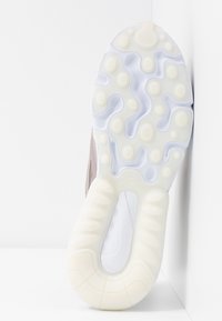 Shoe sole in white rubber with textured patterns; light gray accents. The design features a distinctive cutout shape and rounded details.