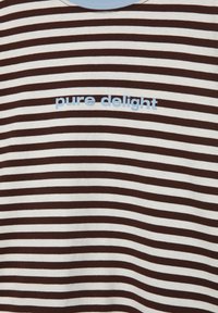 Rjava in bela majica z vodoravnimi črtami in napisom »čista radost« v modri barvi čez prsni del.