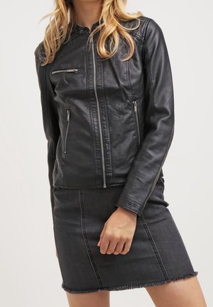 Frau trägt eine schwarze Lederjacke mit Reißverschluss und Reißverschlusstaschen, kombiniert mit einem dunklen Jeansrock mit abgesteppten Nähten und ausgefranstem Saum.