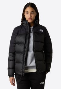 Svart pufferjakke med quiltet design, glidelås lukking, høy krage og elastiske mansjetter. Har "The North Face"-logo på brystet.