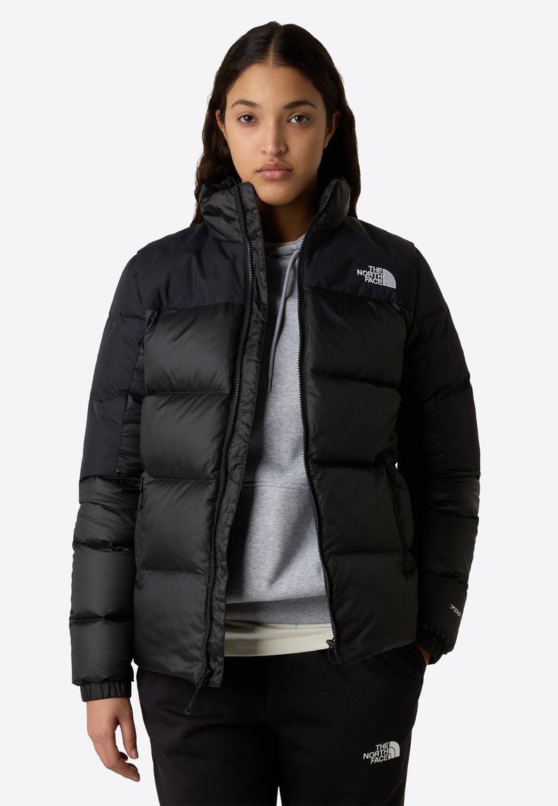 Svart pufferjakke med quiltet design, glidelås lukking, høy krage og elastiske mansjetter. Har "The North Face"-logo på brystet.