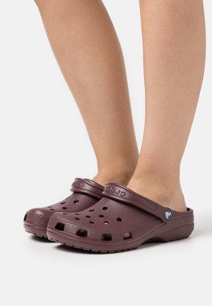 Zoccoli color bordeaux con fori di ventilazione, design slip-on e cinturino posteriore. Realizzati in materiale leggero con suole texture per una migliore aderenza.