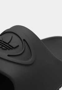 Czarna klapka z gładką, matową fakturą i wypukłym logo na pasku, o szerokim i zaokrąglonym kształcie.