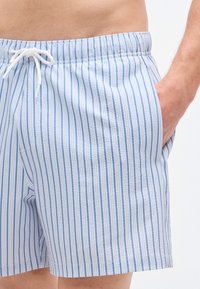 Μπλε και λευκά ριγέ μαγιό σορτς από ελαφρύ ύφασμα με ελαστική μέση και κορδόνι, που διαθέτουν πλαϊνές τσέπες.