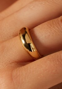Goldring mit einem glatten, abgerundeten Design, das Licht auf einem Hintergrund mit strukturierter Haut reflektiert.