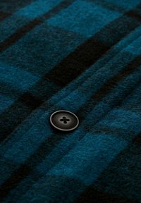 Geruite wollen stof in blauw en zwart tinten, met een ronde zwarte knoop met vier gaten, met een fijne textuur en verticale strepen.