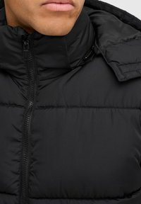 Schwarze Pufferjacke mit hohem Kragen, Reißverschluss vorne und weicher, gesteppten Textur mit horizontaler Naht.