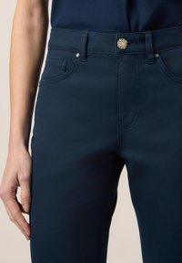 Marineblauwe stretchjeans met een aansluitend ontwerp, voorzakken en een decoratieve knop met een edelsteenteil. Glad textuur en klassieke snit.