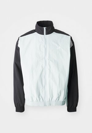 Světle modrá a černá větruodolná bunda s vysokým límcem, zapínáním na zip, elastickými manžetami a bílým logem na prsou.