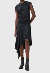 Svart asymmetrisk klänning med en åtsittande livdel, korta ärmar och rynkdetaljer. Har en draperad kjol och en mjuk, slät textur.