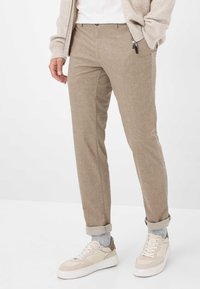 Beige geprinte broek met een subtiele ruitpatroon, rechte snit en opgerolde boorden, gecombineerd met lichte sneakers en een lichtgrijze sok.