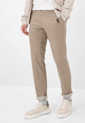 Pantaloni beige a motivo con un sottile motivo a quadri, taglio dritto e orli risvolti, abbinati a sneakers chiare e a un calzino grigio chiaro.
