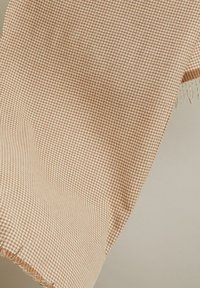 Tissu tissé en beige clair avec un motif à petits carreaux, présentant des bords frangés pour plus de texture. Design bicolore avec une finition douce.