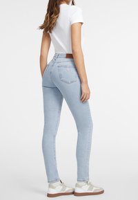 Slim-fit ljusblå jeans med hög midja, med en brun läderlapp på baksidan och en logotypdetalj på fickan. Matchas med vita sneakers.