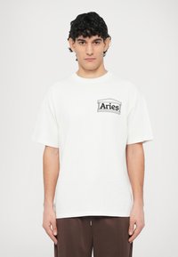 T-shirt en coton blanc à manches courtes, avec un logo graphique noir sur le côté gauche de la poitrine. Coupe standard, col rond.