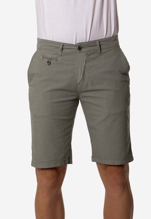 Pantalones cortos de hombre en verde oliva, hasta la rodilla, con cierre de botón y bolsillos delanteros, combinados con una camisa blanca metida dentro del pantalón.