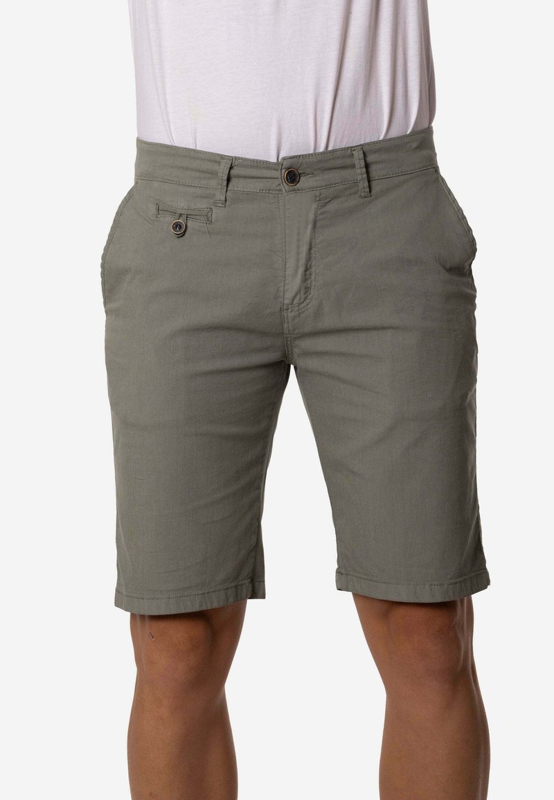 Pantalones cortos de hombre en verde oliva, hasta la rodilla, con cierre de botón y bolsillos delanteros, combinados con una camisa blanca metida dentro del pantalón.