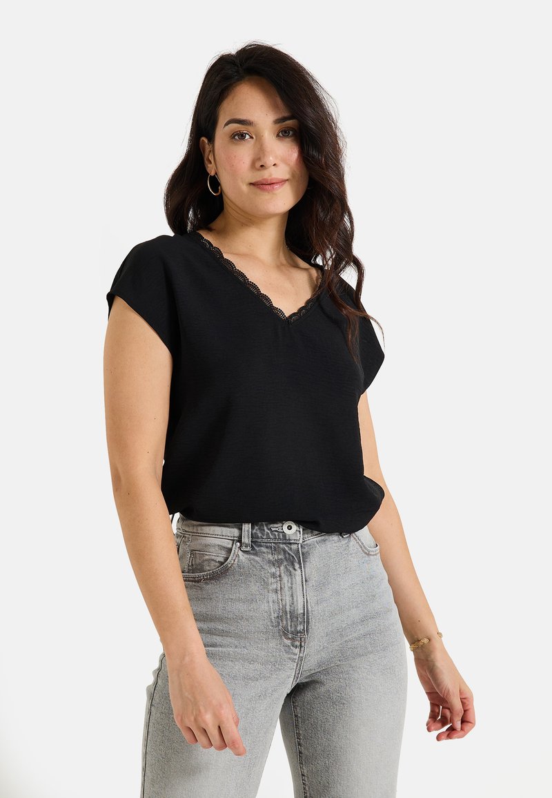 Top negro de manga corta con escote en V y borde de encaje. Combinado con jeans de cintura alta en gris claro, que presentan un ajuste relajado y una apariencia casual.