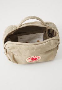 Bustina beige Fjällräven Kånken aperta con nome e biglietto da visita visibili all'interno su uno sfondo bianco.