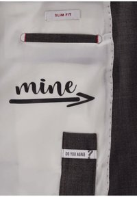 Futter eines Slim-Fit-Sakko mit einem Stoffetikett, auf dem "DO YOU AGREE?" steht, und bedrucktem Text "mine" mit einem Pfeil nach rechts.