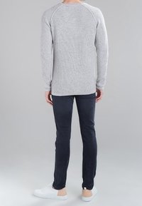 Grijze geribbelde trui met lange mouwen en raglanmouwen, gecombineerd met donkere slim-fit jeans en witte sneakers. Achteraanzicht, minimalistisch ontwerp.