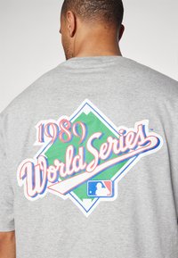 Camiseta de manga corta gris con un gráfico colorido de "Serie Mundial 1989" dentro de una forma de diamante verde en la parte posterior.