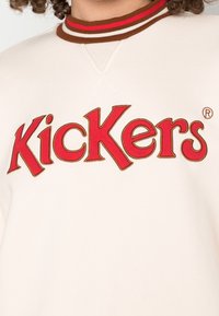 Felpa crema con colletto tondo, caratterizzata da un colletto a strisce marroni e rosse e da un grande logo ricamato rosso "Kickers".