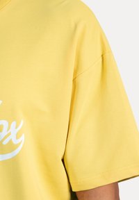 Geel katoenen t-shirt met een relaxed fit, voorzien van korte mouwen en een wit grafisch ontwerp op de voorkant. Glad oppervlak en eenvoudige stiksels.