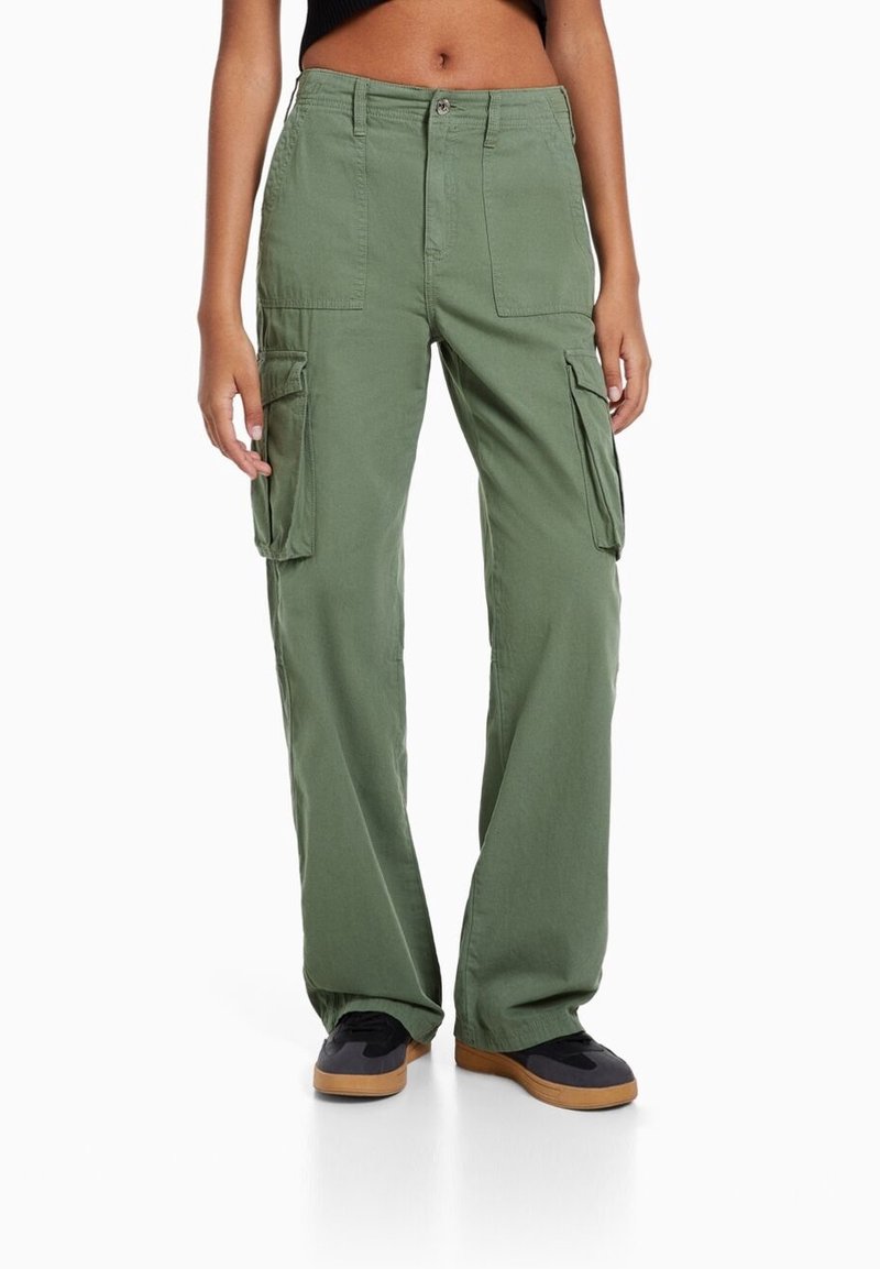 Zielone spodnie cargo wykonane z bawełny o luźnym kroju, z wieloma kieszeniami bocznymi i zapięciem na guziki. W połączeniu z czarnymi trampkami.
