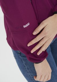 Paarse waterdichte jas met elastische manchetten, voorzien van de borduring "WPRO 8000" op de linkermouw. Gladde textuur, ontworpen voor gebruik in de buitenlucht.