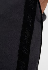 Acercamiento de una tela negra con una franja vertical de terciopelo negro que presenta un sutil texto en cursiva a lo largo del borde.