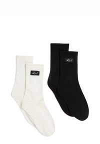 Dwie pary prążkowanych skarpet; jedna biała i jedna czarna. Każda para ma czarną etykietę z białym napisem. Miękki materiał, wygodny fason.